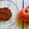 tomato powder in a glass dish next to fresh tomatoes