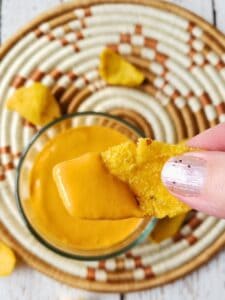 a hand holding a corn chip dipped in dairy free cheese sauce