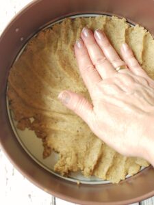 a hand pressing a crust into a springform pan