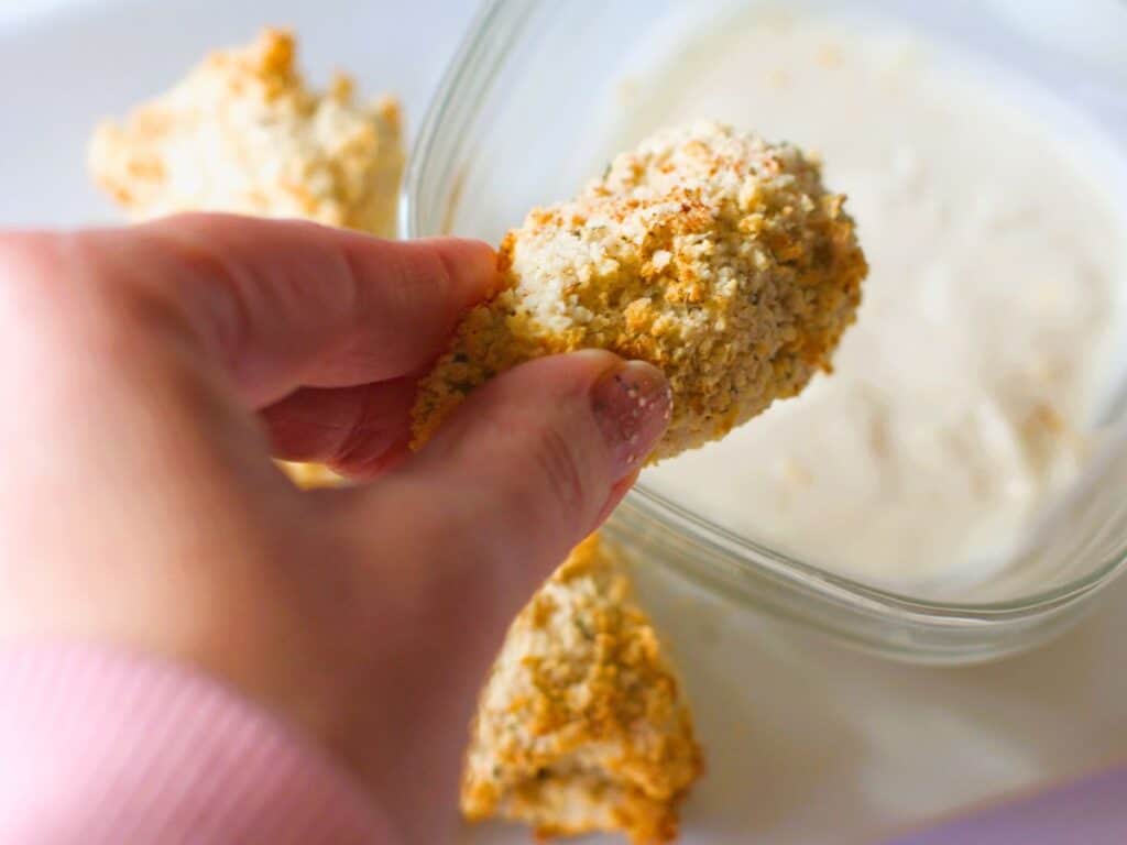 a hand dipping an air fryer artichoke into dipping sauce