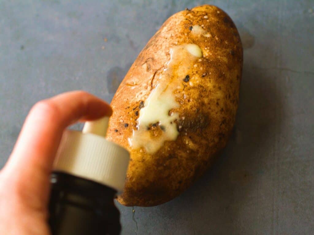 olive oil being sprayed onto a potato