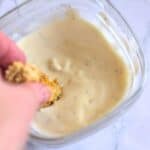 a hand dipping air fried artichokes into yogurt sauce