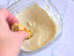 a hand dipping air fried artichokes into yogurt sauce