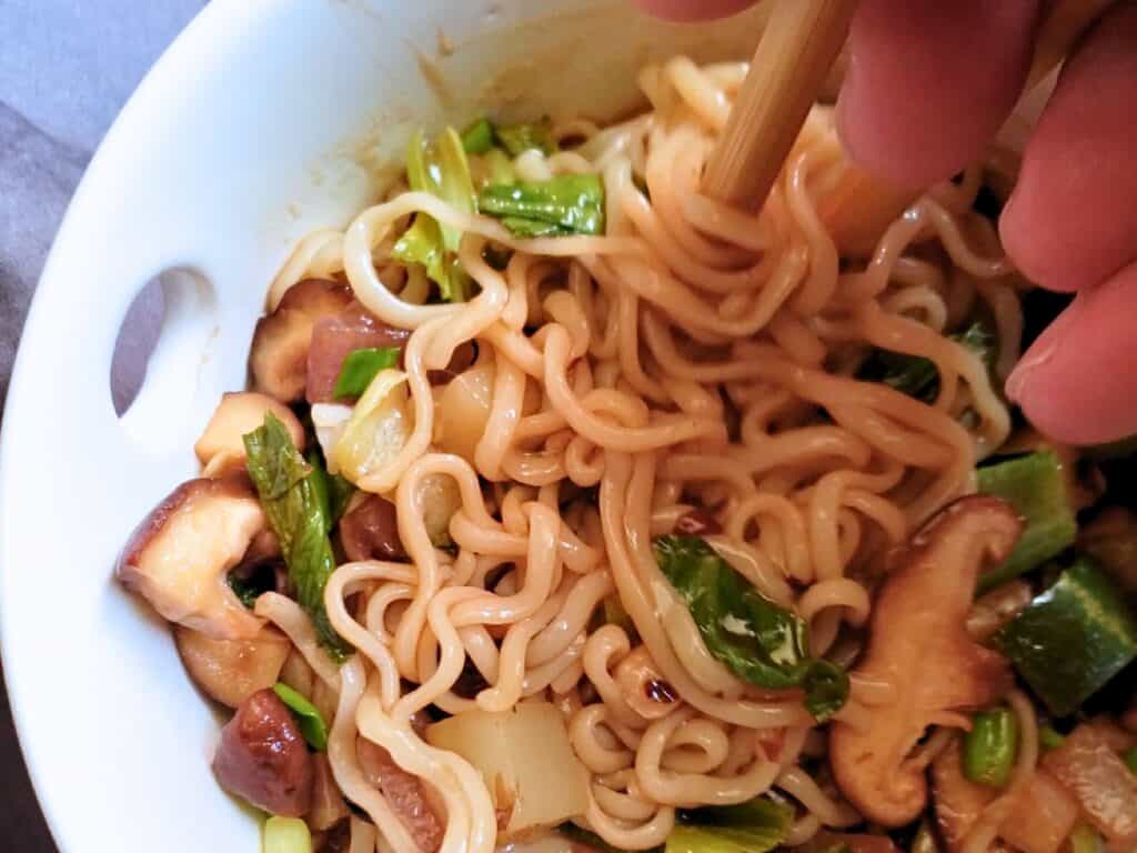 a hand holding chopsticks picking up ramen noodles