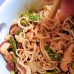 a hand holding chopsticks picking up ramen noodles