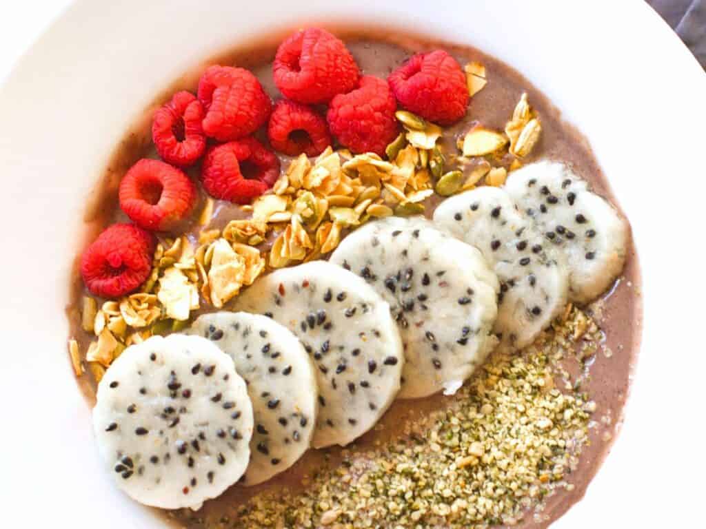 a smoothie bowl with dragon fruit, raspberries, and granola