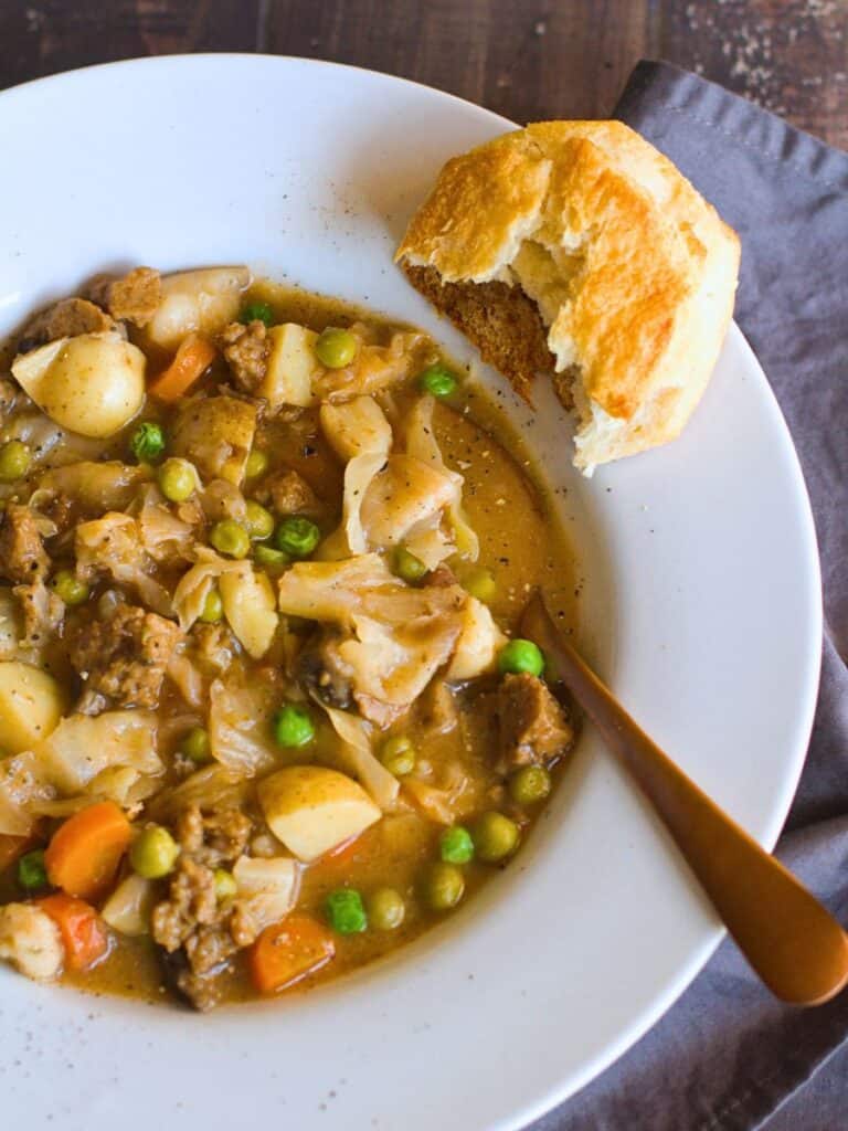 vegan stew in a white bowl with a biscuit