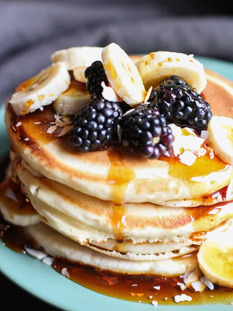 dairy free pancakes on a plate covered in maple syrup and fresh fruit