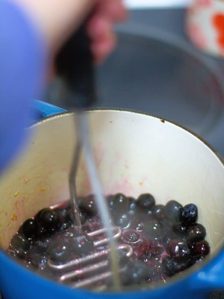 a potato masher mashing blueberries for a compote
