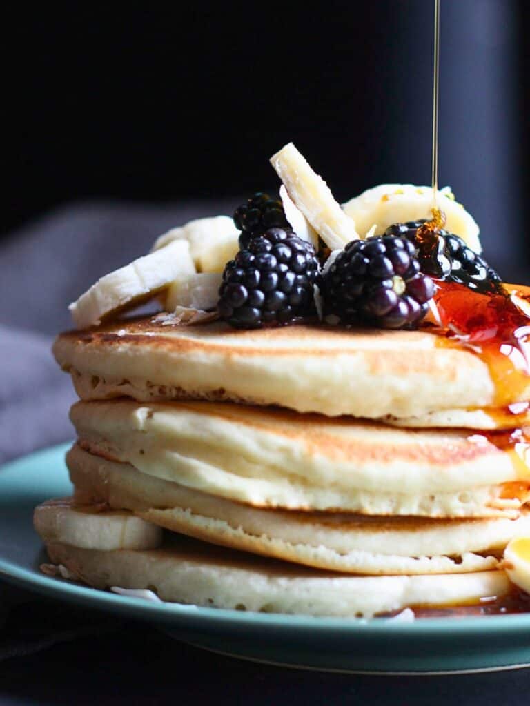 maple syrup being poured over pancakes with fruit