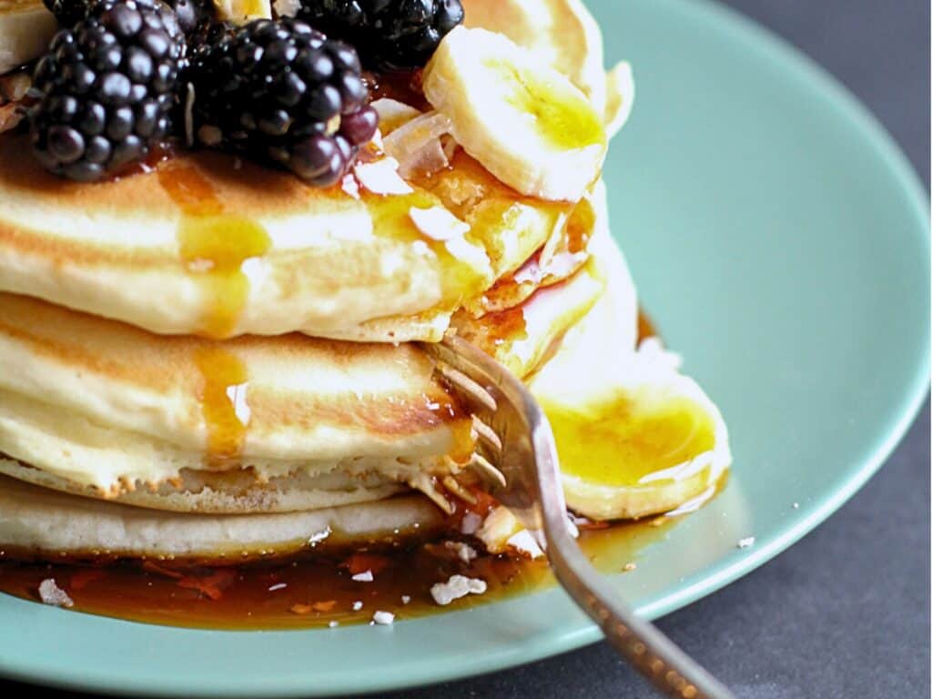 a stack of pancakes with bananas and blackberries