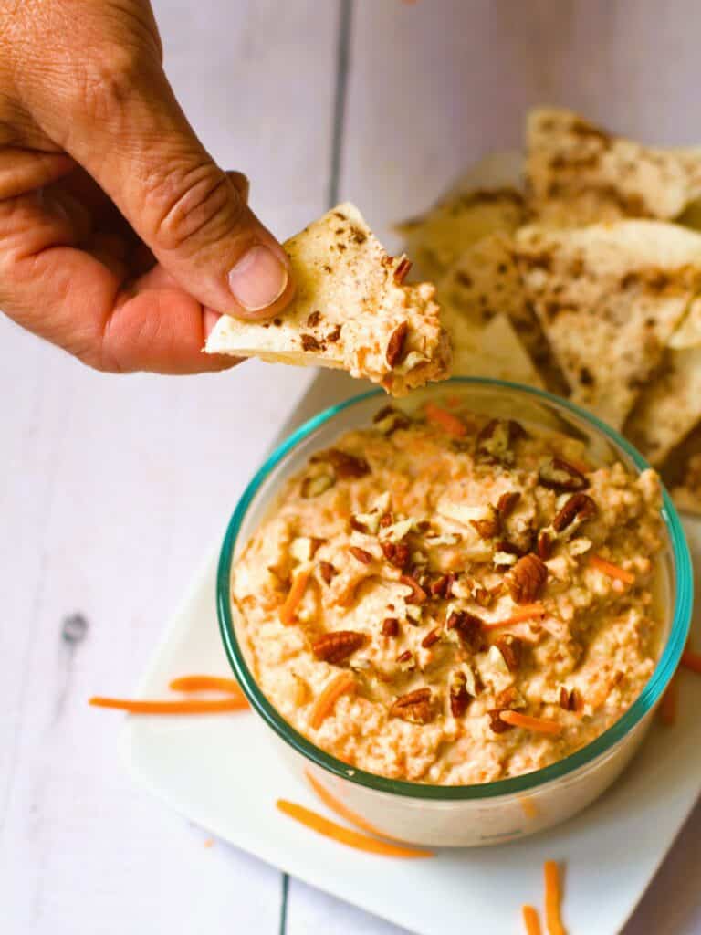 a hand dipping carrot cake vegan dip