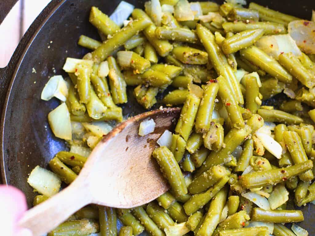 a hand with a spoon stirring green beans