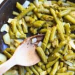 a hand with a spoon stirring green beans