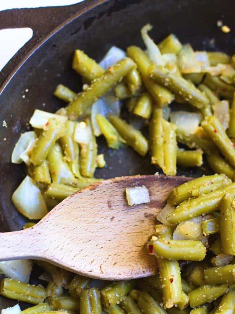 a wooden spoon in a skillet of cooked canned green beans