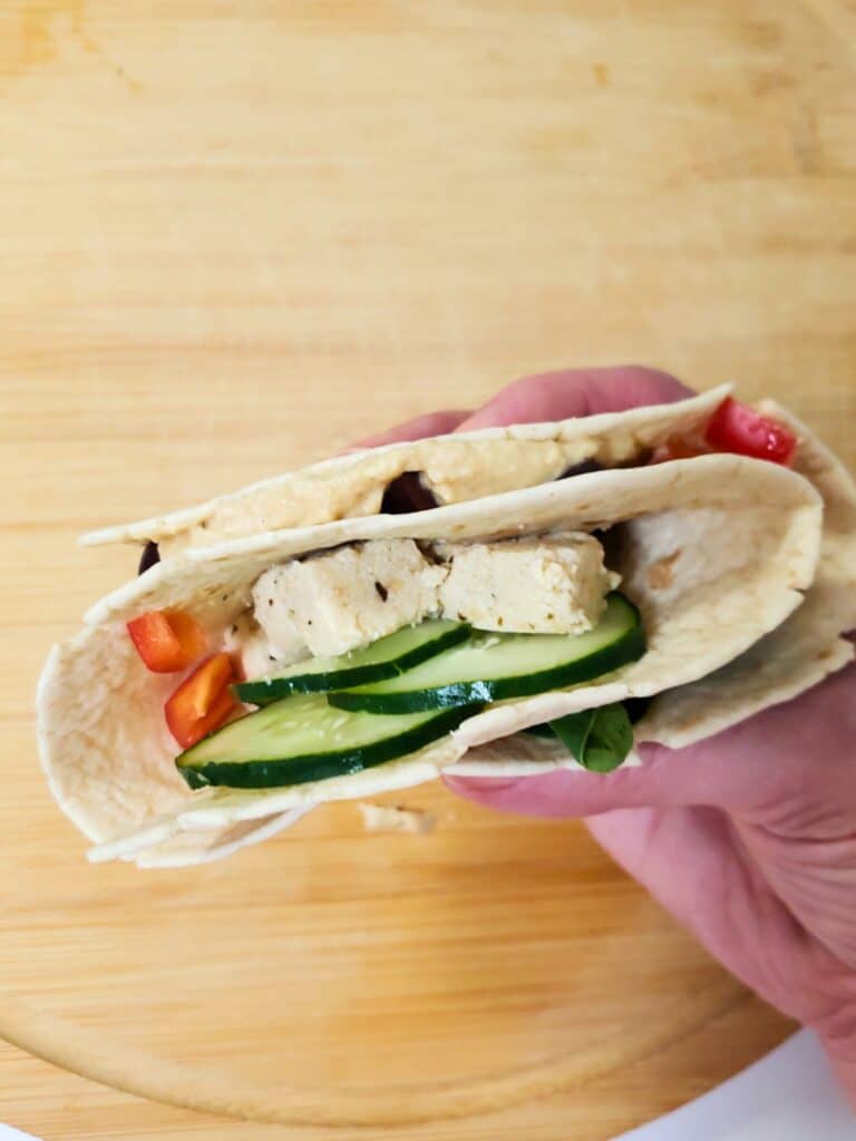 a hand holding a hummus wrap