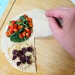 a hand folding a hummus wrap into a triangle