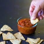 a hand dipping a keto tortilla chip into salsa