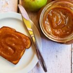 apple butter on a piece of toast with a jar of apple butter and apples next to it