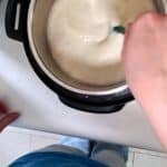 a hand stirring the yogurt mixture in an instant pot