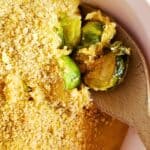 brussels sprouts casserole with dairy free cheese in a white dish with a wooden spoon