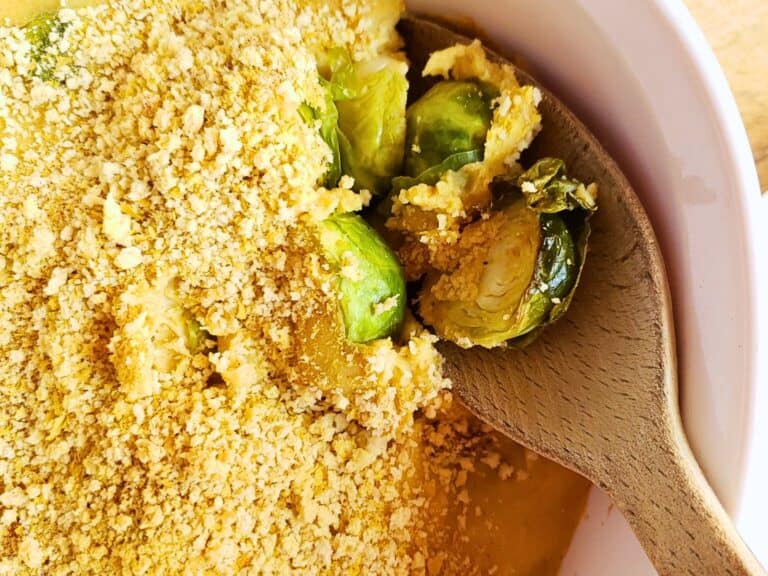 brussels sprouts casserole with dairy free cheese in a white dish with a wooden spoon