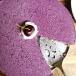 Slice of high-protein vegan blueberry cheesecake on a plate, dairy-free with a date-oat crust and cocoa whip on top.