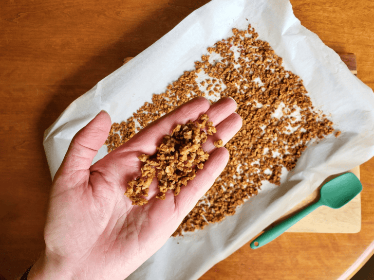 a hand holding vegan bacon bits over a pan of plant based bacon bits